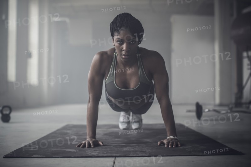 Black woman doing push-ups in dark gym