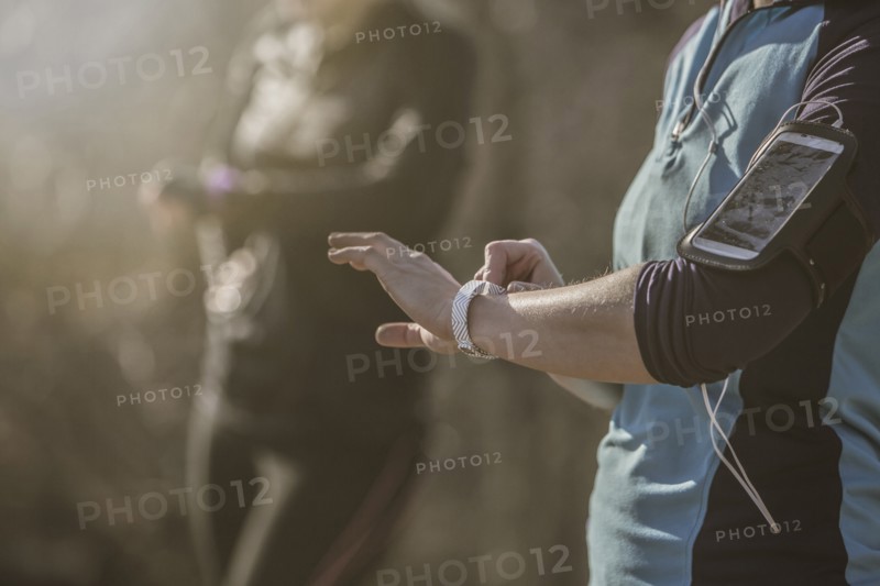 Caucasian runners checking fitness watches in forest