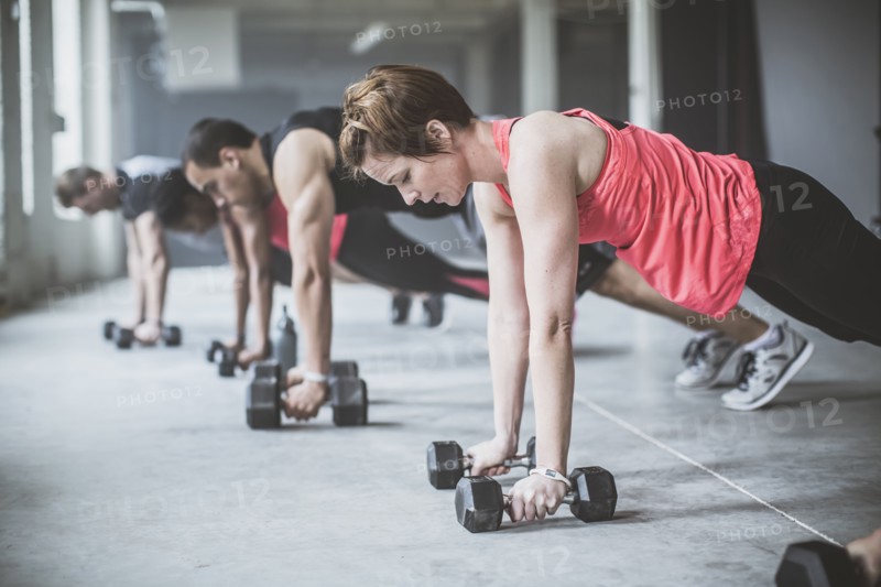 Athletes doing push-ups with dumbbells on floor