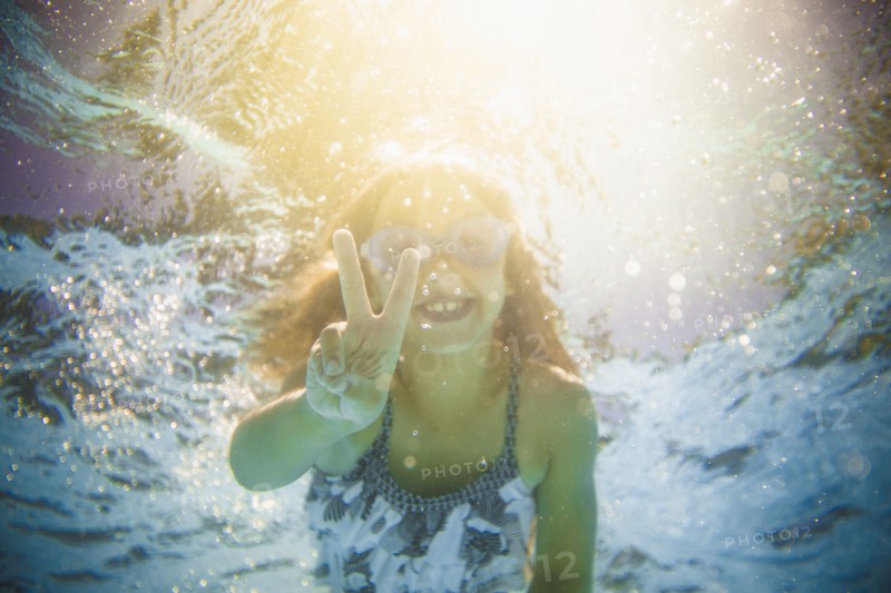 Caucasian girl swimming underwater gesturing peace sign
