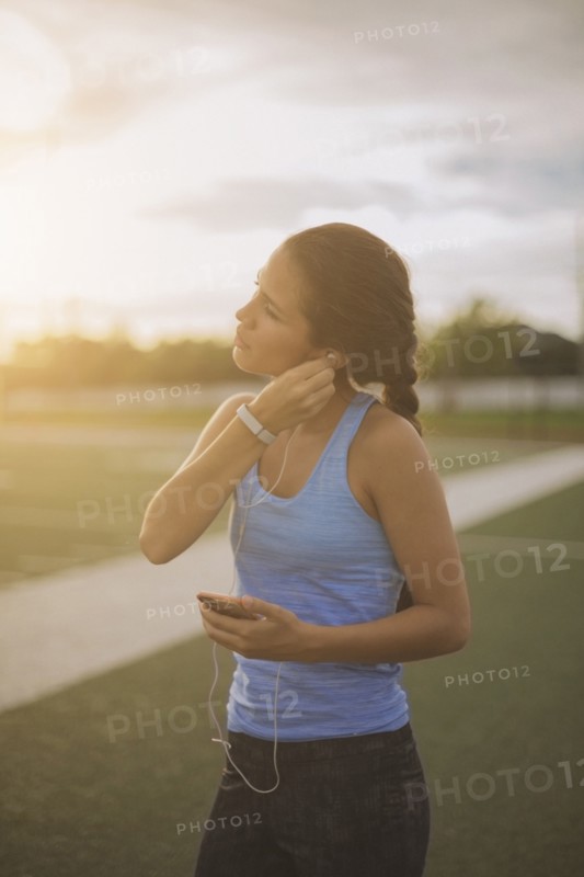 Mixed race athlete listening to mp3 player on sports field
