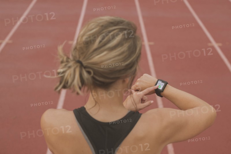 Caucasian runner checking watch on sports field