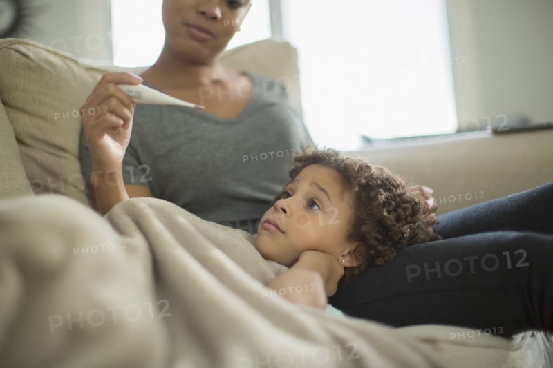 Mother measuring temperature of daughter on sofa