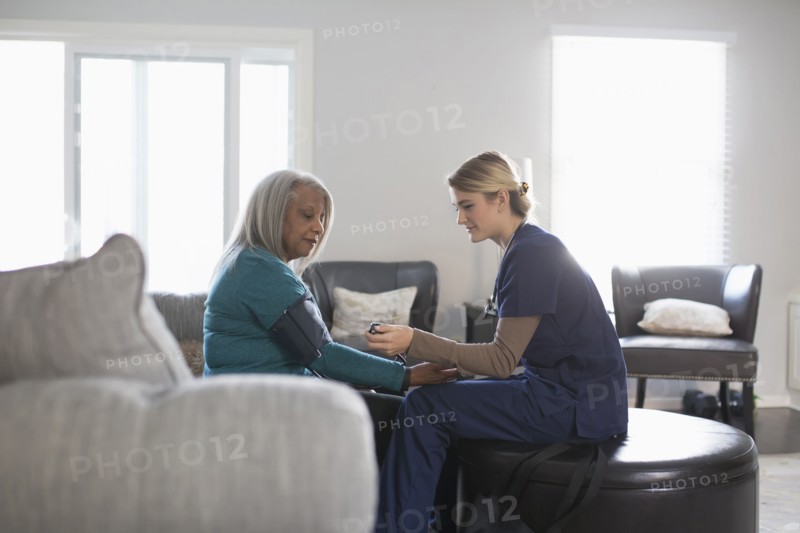 Nurse taking patient blood pressure in living room