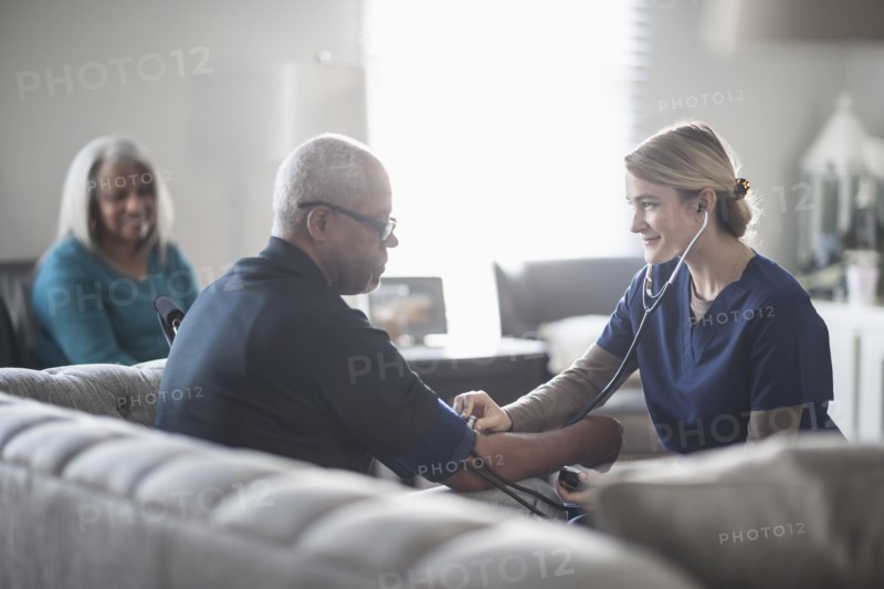 Nurse taking patient blood pressure in living room