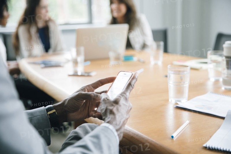 Businessman texting on cell phone in meeting