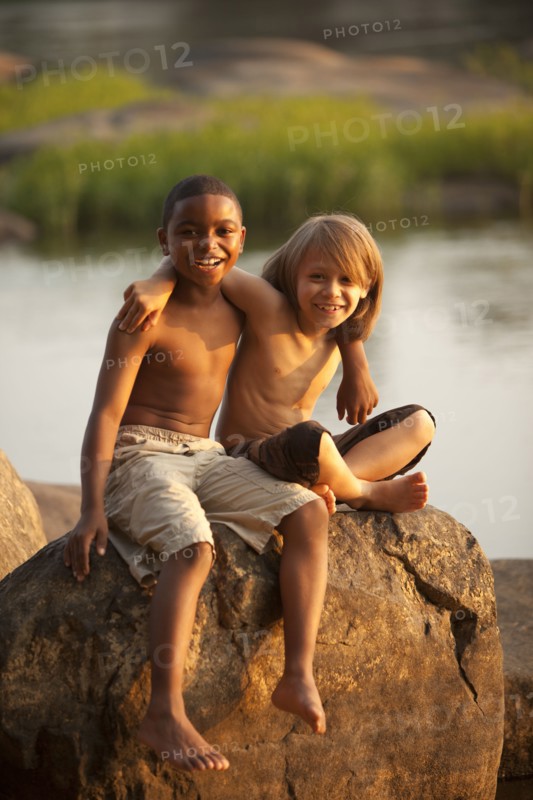 Smiling boys hugging on rock near lake