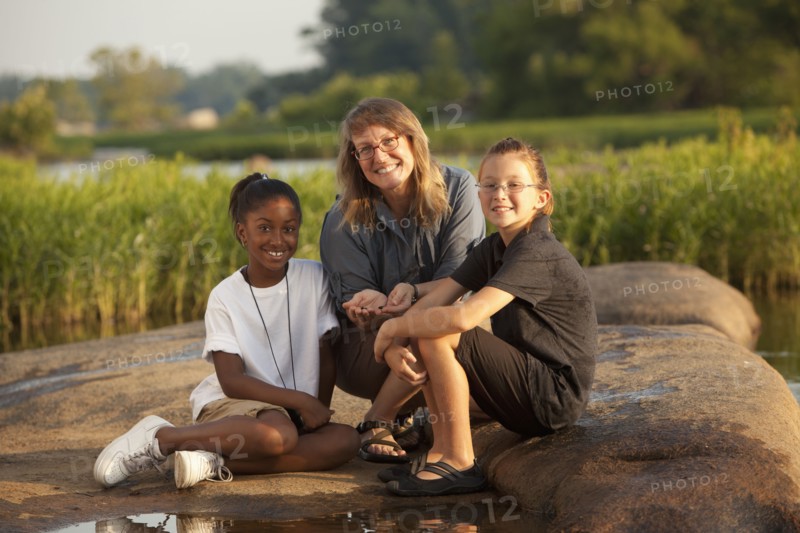 Teacher and students sitting on rock near river