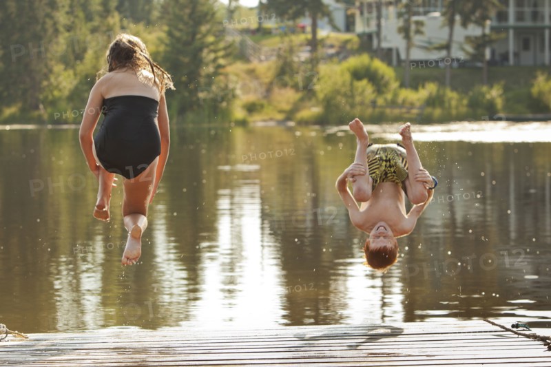 Caucasian children jumping into lake