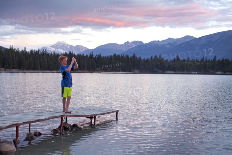 Caucasian boy standing on wooden dock photographing lake