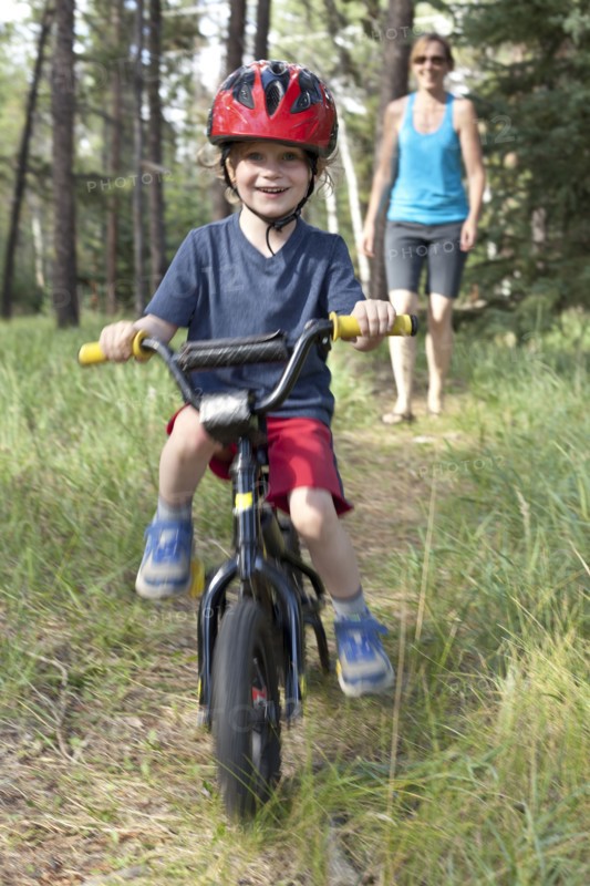 Caucasian mother watching smiling son on bicycle