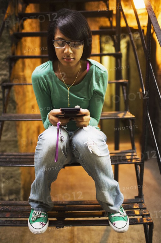Hispanic girl text messaging on staircase