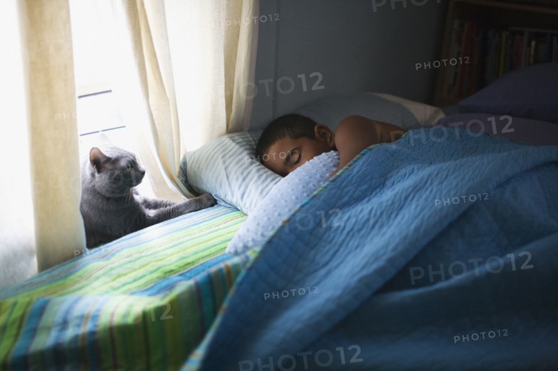 Mixed race boy sleeping in bed with cat