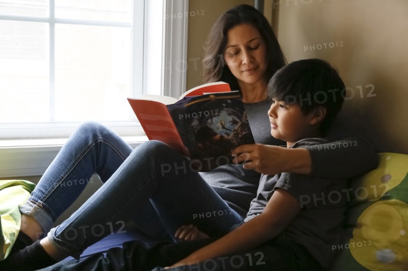 Mother and son reading book near window