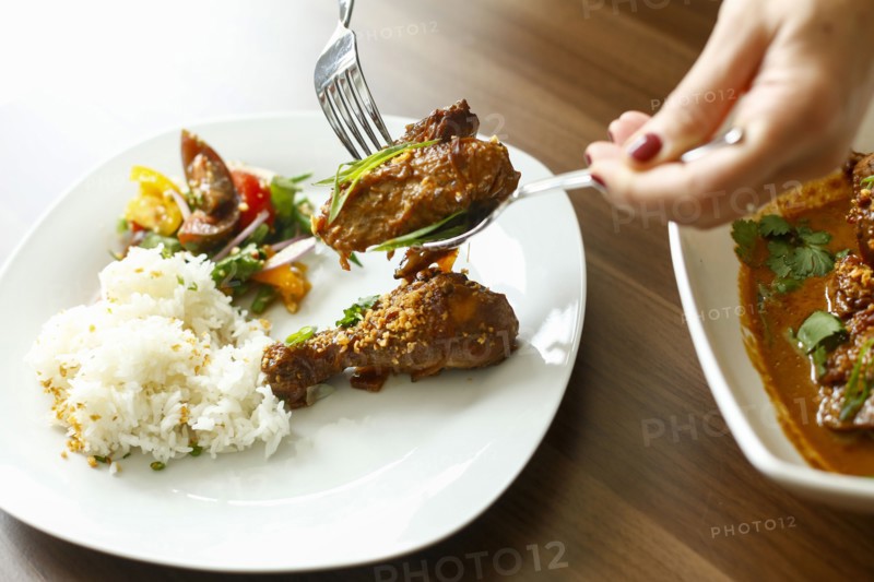 Woman holding meat over plate with fork and spoon