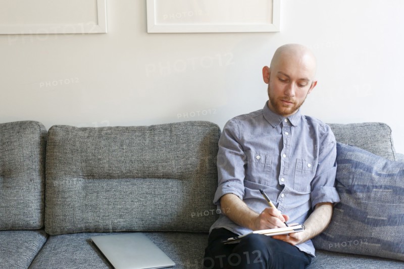 Caucasian man sitting on sofa writing in notepad