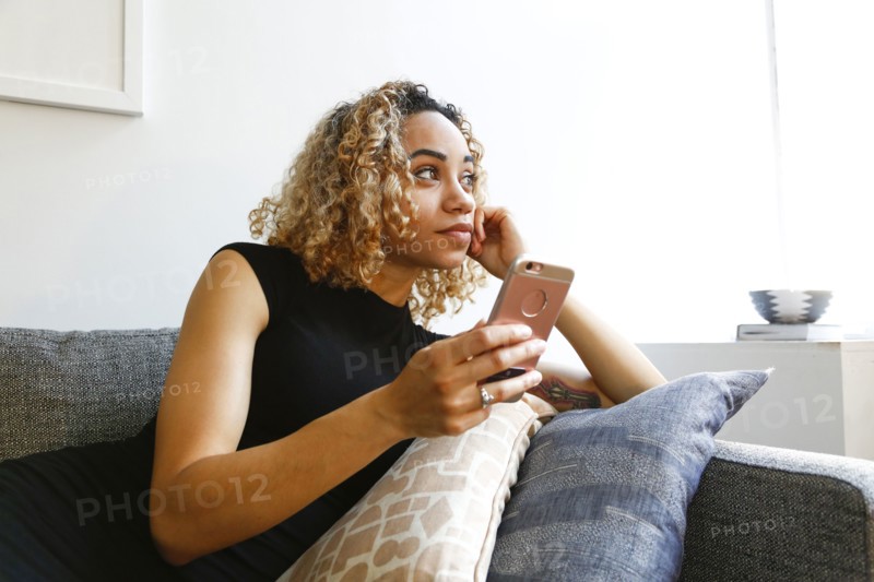 Mixed race woman laying on sofa holding cell phone