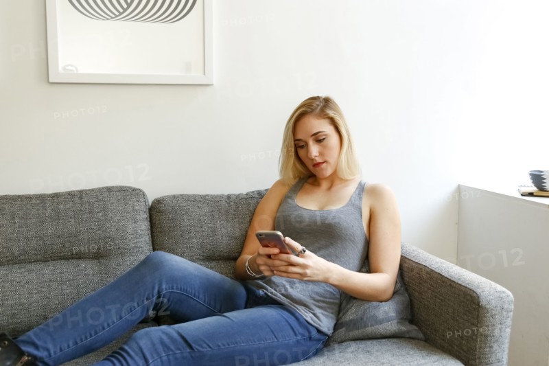 Caucasian woman sitting on sofa texting on cell phone
