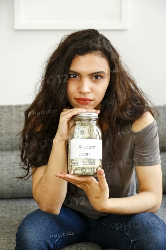 Portrait of mixed race woman holding jar of money for student loan