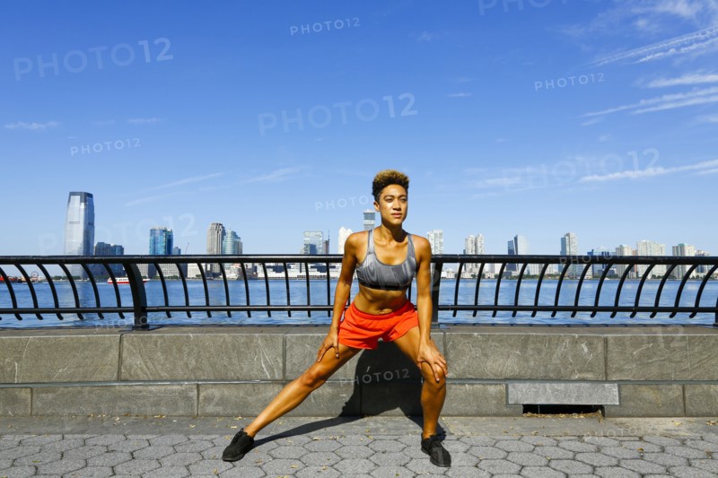 Mixed race woman stretching legs at waterfront