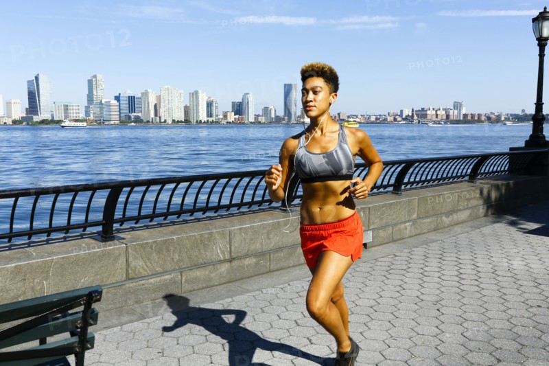 Mixed race woman running at waterfront listening to earbuds