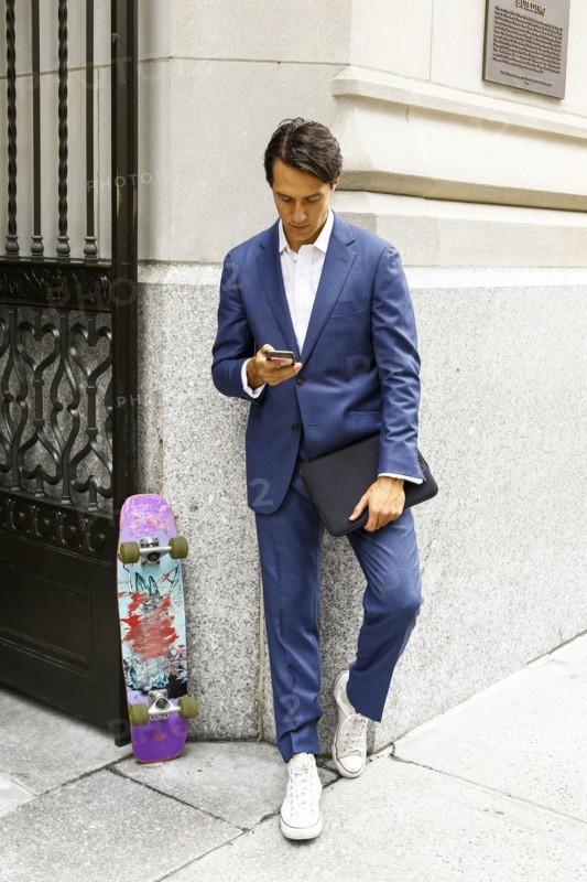 Caucasian businessman with skateboard texting on cell phone