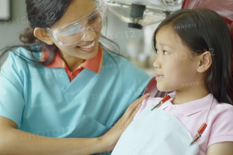 Indian female dental assistant smiling at young Asian female patient
