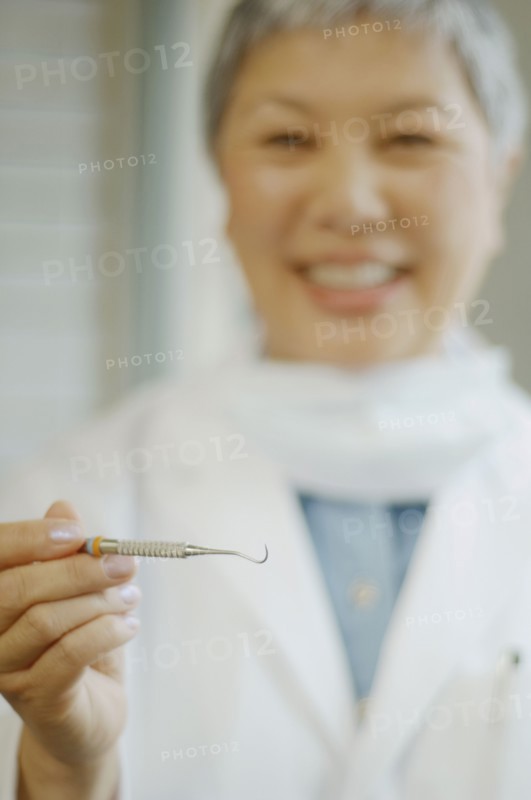 Senior Asian female dentist holding up dental tool