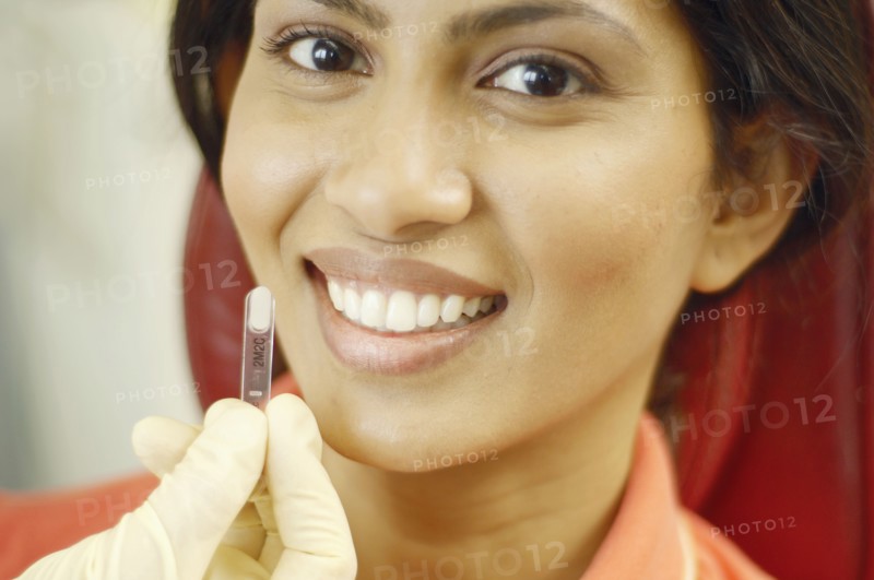 Tooth color sample being held up next to Indian woman's teeth