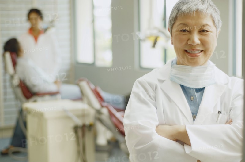 Senior Asian female dentist with assistant and patient in background