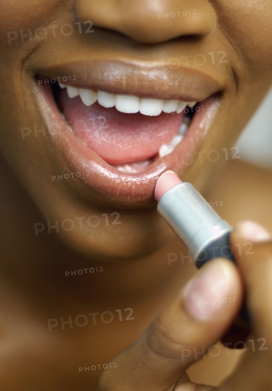 Close up of African woman applying lipstick