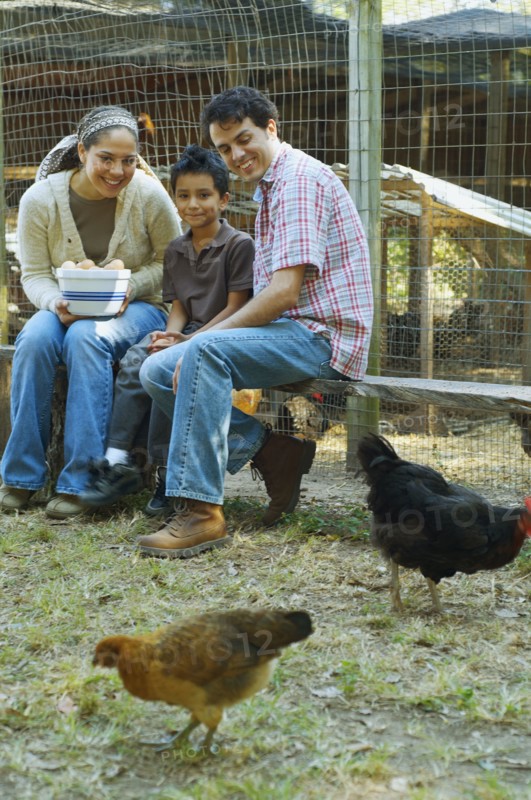 Multi-ethnic family holding bowl of eggs next to chickens