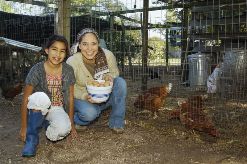 Hispanic mother and daughter with bowl of eggs next to chickens