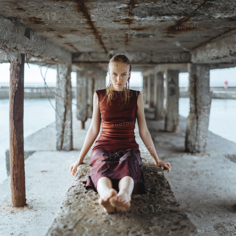 Caucasian girl wearing wet dress sitting underneath dock