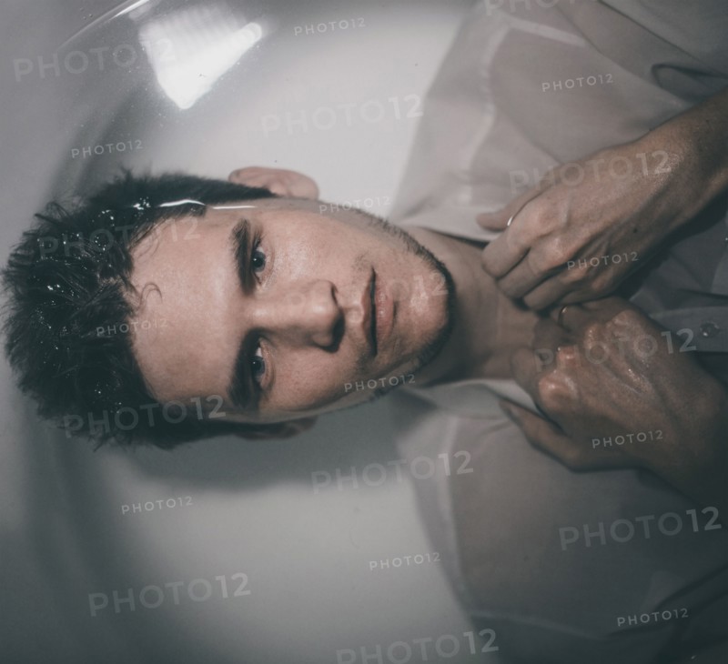 Caucasian man wearing shirt laying underwater in bathtub