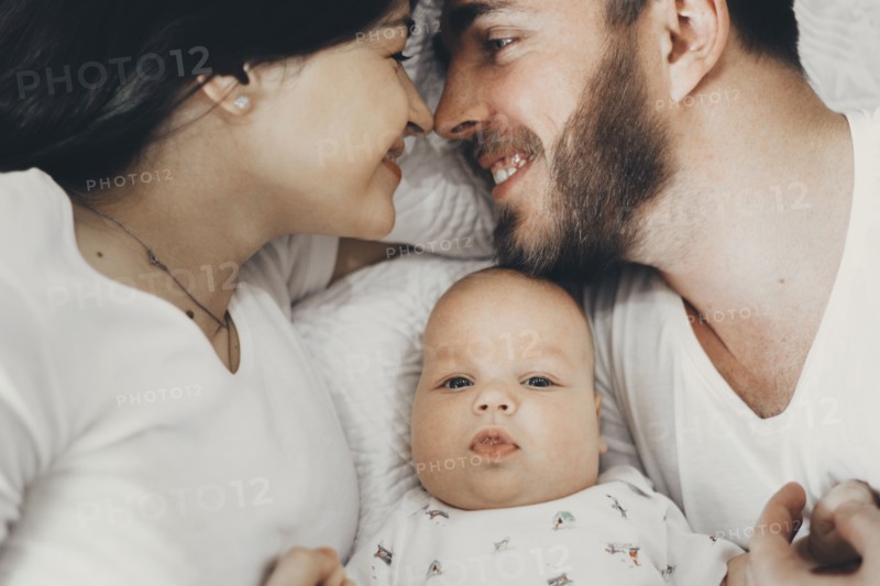 Caucasian mother and father laying on bed with baby son