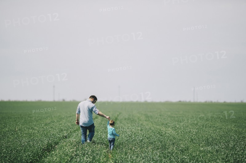 Caucasian father and son holding hands and walking in field