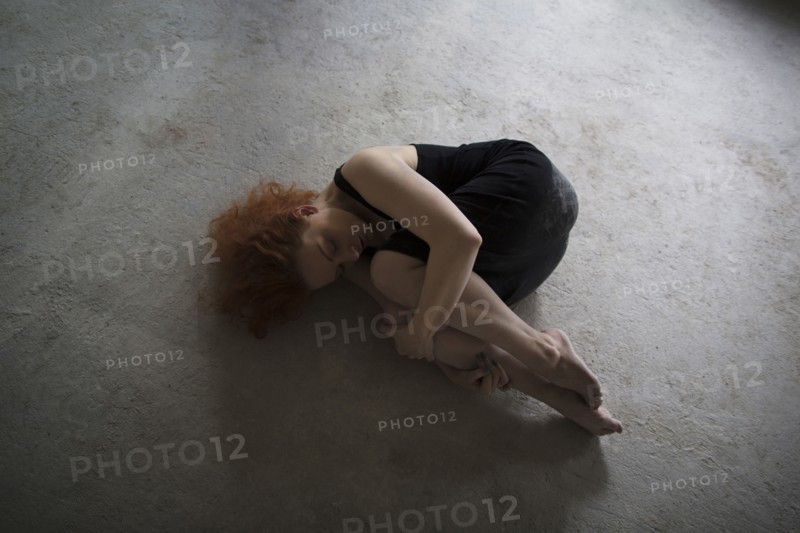 Caucasian woman laying on concrete in fetal position
