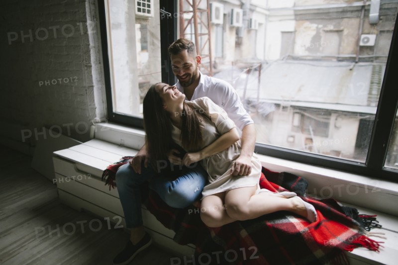 Caucasian couple cuddling on bench near window