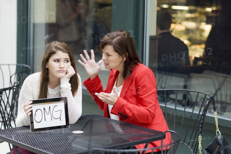 Caucasian girl with tablet as mother chastises her at cafe