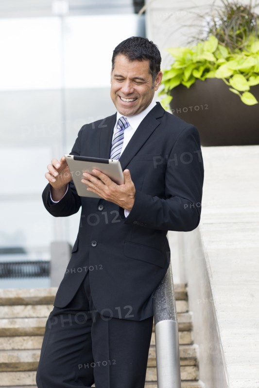 Hispanic businessman with tablet computer on city street