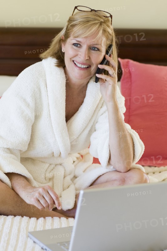 Caucasian woman talking on cell phone on bed