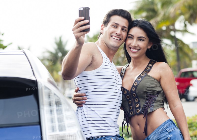Hispanic couple taking cell phone selfie outdoors
