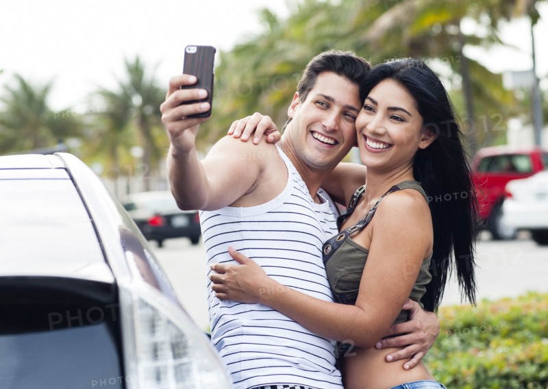 Hispanic couple taking cell phone selfie outdoors