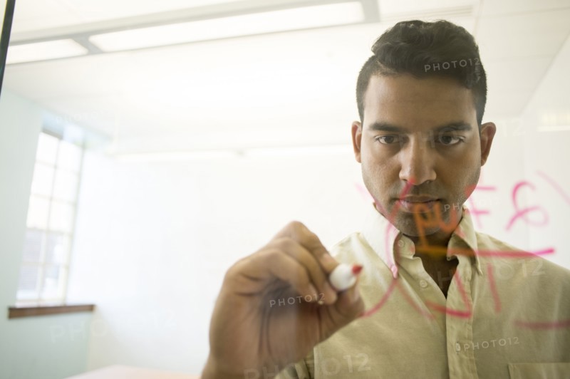 Asian businessman writing on glass window in office