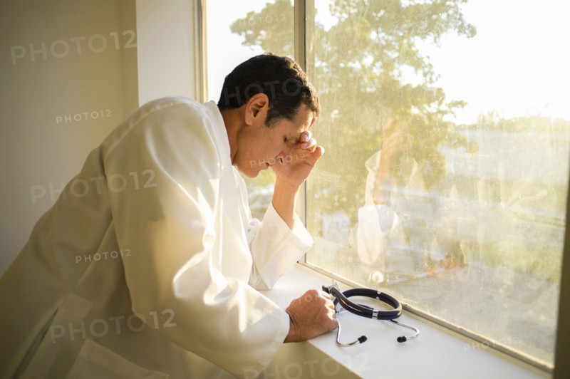 Stressed Hispanic doctor standing at window