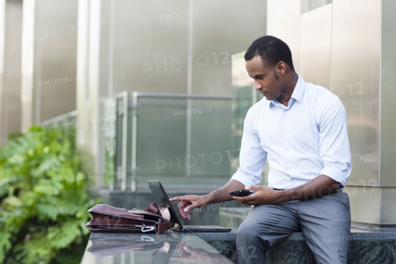 Black businessman using laptop outside building