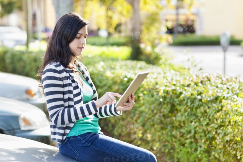 Hispanic woman using digital tablet in parking lot