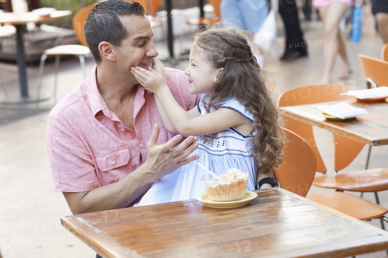 Hispanic father and daughter eating at sidewalk cafe