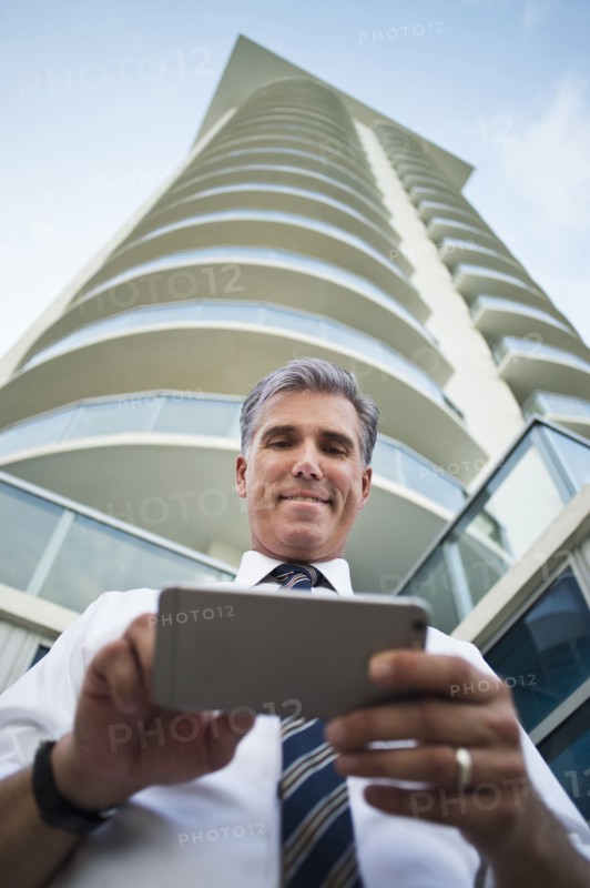 Low angle view of Caucasian businessman using cell phone at high rise building